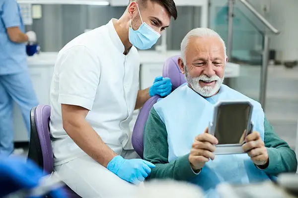 Happy, senior patient looking at himself in a mirror with his new dental implants at San Francisco Dental Arts in San Francisco, CA