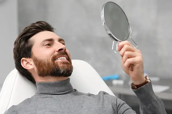 Smiling dental patient leaning back in exam chair and looking up into mirror at his new dental implants at San Francisco Dental Arts in San Francisco, CA