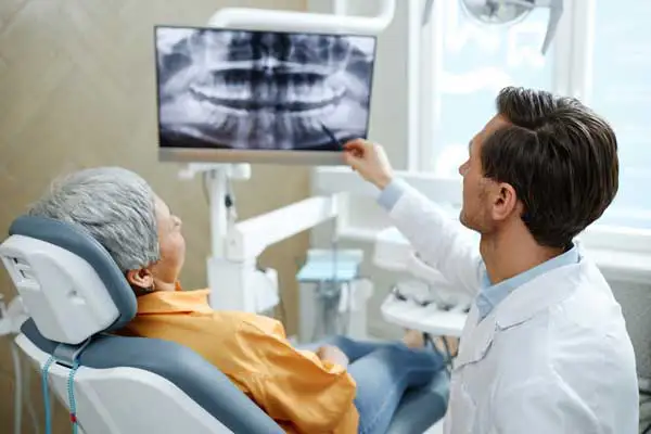 Back view of male dentist pointing at tooth X-ray image on screen during dental implant consultation at San Francisco Dental Arts in San Francisco, CA