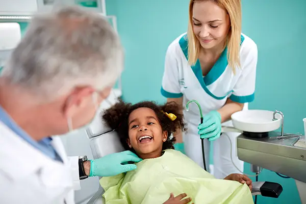 Adorable and young Black girl sitting in a dental chair and smiling at her dentist and assistant at San Francisco Dental Arts in San Francisco, CA