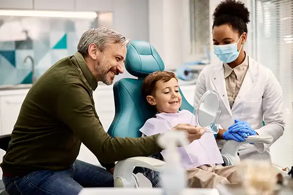 Father holding a mirror for his happy, young son sitting in a dental chair at San Francisco Dental Arts in San Francisco, CA